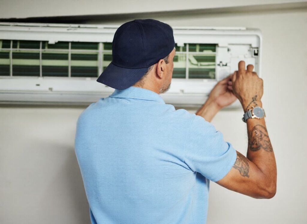 Technician repairing an air conditioner from the back, using tools to service HVAC and electrical components