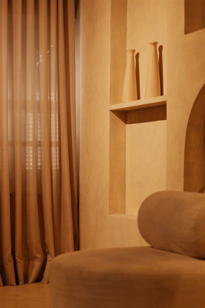 Warm terracotta-toned living room with curtains, an alcove shelf with vases, and a sofa